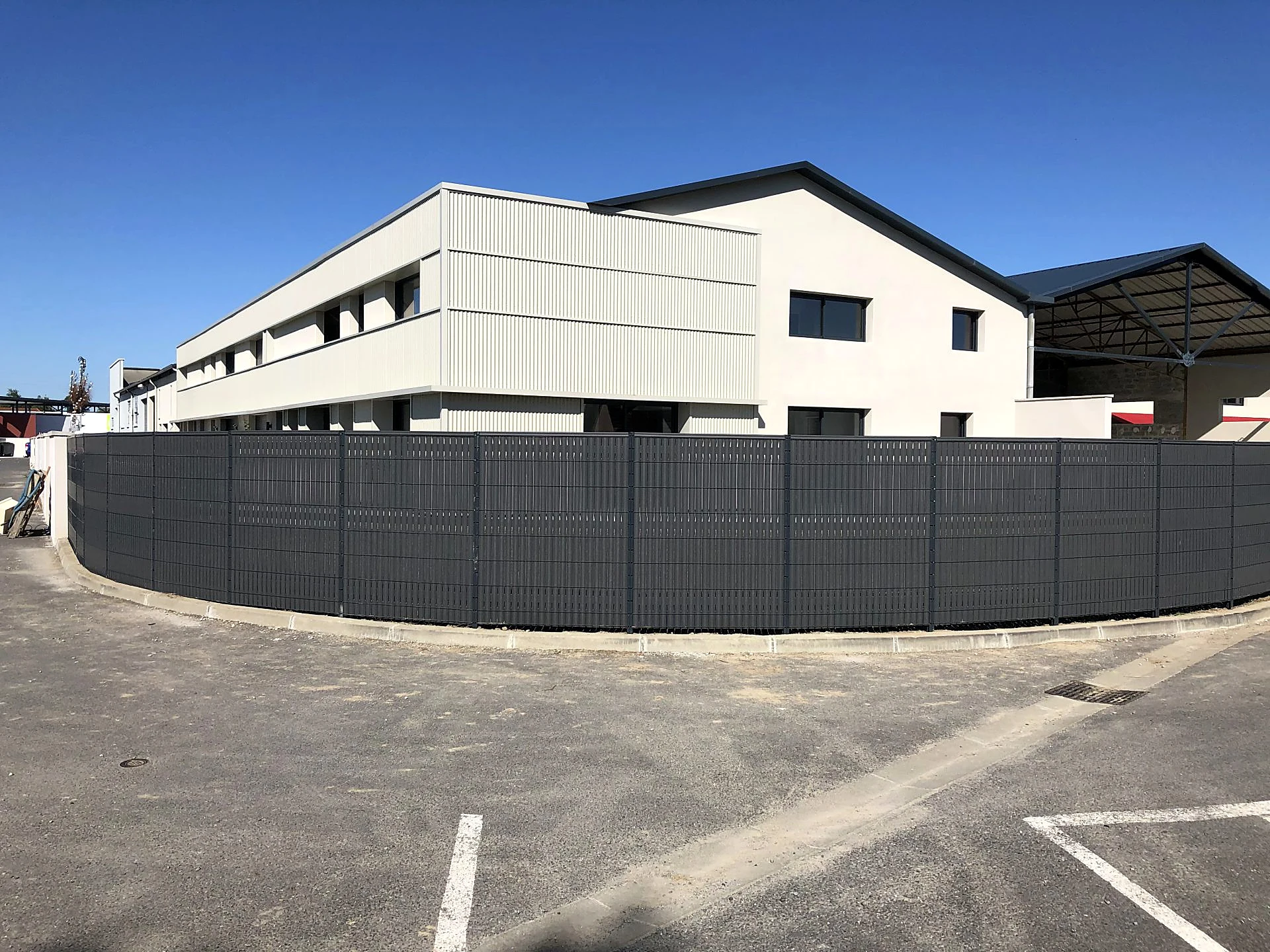 Clôture occultée suivant la courbe d’un parking de bâtiment d’activité